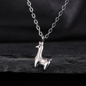 May include: A silver chain necklace with a small silver llama pendant. The necklace is on a black background.