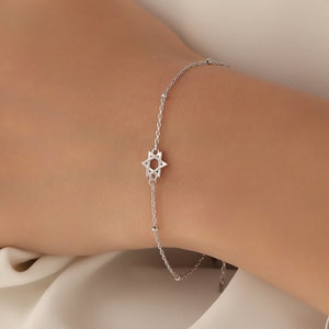 Op de afbeelding: Een delicate zilveren kettingarmband met een kleine, gedetailleerde Davidster-bedel. De armband is verstelbaar en heeft een eenvoudig, elegant ontwerp.