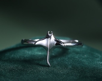 Könnte beinhalten: Ein silberner Ring mit einem Manta-Rochen-Design. Der Ring liegt auf einem grünen Samtstoff.