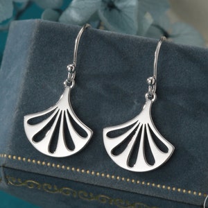 May include: A pair of silver earrings with a fan-shaped design. The earrings are hanging from a blue velvet box.