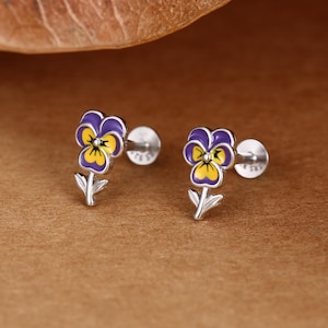 Peut inclure: Une paire de boucles d'oreilles à tige représentant une pensée avec des pétales en émail violet et jaune et des tiges argentées. Chaque boucle possède un fermoir circulaire plat et une tige, avec un petit poinçon gravé sur le métal.