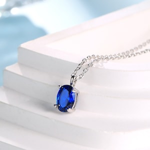 Puede incluir: Un collar de cadena de plata con un colgante ovalado azul.