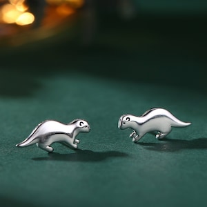 Pode incluir: Um par de brincos de prata com um pequeno design de lontra. As lontras estão viradas em direções opostas e têm um estilo simples e minimalista.