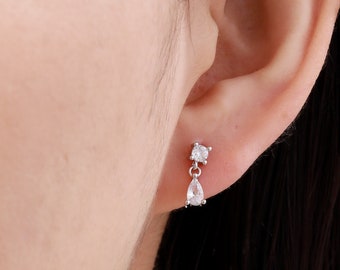 May include: A pair of silver earrings with a teardrop-shaped crystal dangling from a smaller round crystal.
