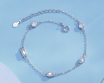 Puede incluir: Un brazalete de cadena de plata con cinco piedras de cristal transparentes. Las piedras son de diferentes formas, incluyendo redonda, ovalada y rectangular.