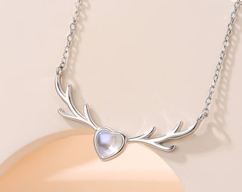 May include: A silver necklace featuring a heart-shaped moonstone pendant and a delicate chain. The pendant is surrounded by two silver antlers.