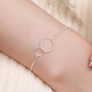 May include: A silver chain bracelet with two interlocking circles. The bracelet is on a person's wrist.