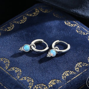 Könnte beinhalten: Ein Paar silberne Creolen mit einem kleinen blauen Opal, der an jeder Creole baumelt.