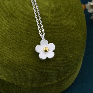 May include: A silver chain necklace with a white flower pendant. The flower has a gold center.