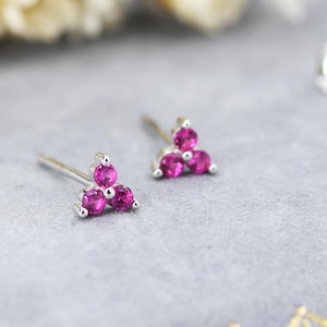 May include: A pair of silver stud earrings with three pink gemstones arranged in a triangular shape.
