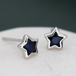 Könnte beinhalten: Ein Paar silberne Stern-Ohrstecker mit blauen Kristall-Zentren.