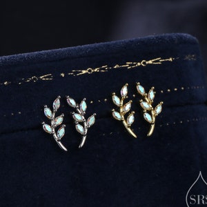 May include: A pair of earrings with a delicate branch design featuring iridescent marquise-shaped stones. The earrings are displayed on a dark blue velvet background.
