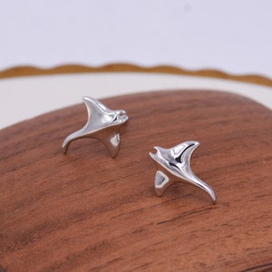 May include: A pair of silver-toned earrings shaped like manta rays. The earrings are small and delicate, and they are perfect for adding a touch of whimsy to any outfit.