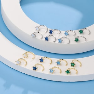 May include: A set of 18 nose rings with star-shaped gemstones. The rings are available in silver and gold with blue, green, and white gemstones.