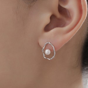 May include: Silver earrings with a pearl in the centre of a wavy, irregular circle.