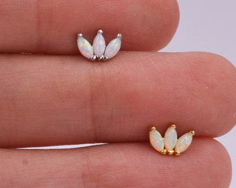 Puede incluir: Dos pequeños pendientes decorativos, uno en metal plateado y otro en metal dorado. Cada pieza presenta tres ópalos blancos de talla marquesa dispuestos en forma de abanico, mostrando destellos iridiscentes sobre la base metálica.