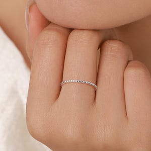Könnte beinhalten: Ein zarter Silberring mit einem strukturierten, perlenbesetzten Design. Der Ring ist dünn und sitzt auf einem Finger, wodurch seine komplizierten Details zur Geltung kommen. Das Design des Rings weist kleine, gleichmäßig verteilte Perlen auf, die einen subtilen, eleganten Look erzeugen. Feinschmuck.