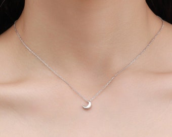 May include: A silver crescent moon pendant necklace on a silver chain. The necklace is worn by a person with fair skin.