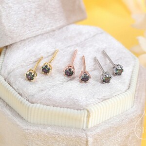 May include: Three pairs of small stud earrings with iridescent gemstones in a white velvet box. The earrings are in gold, rose gold, and silver.