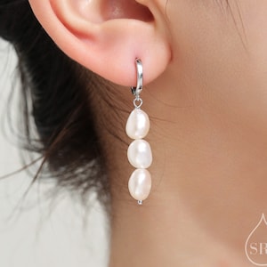 Peut inclure: Boucles d'oreilles créoles en argent avec une chaîne pendante de trois perles blanches.