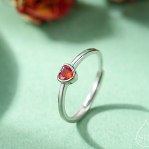 May include: A silver ring with a small red heart-shaped gemstone.