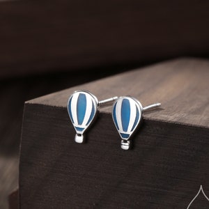 May include: A pair of silver stud earrings with a blue and white enamel hot air balloon design.