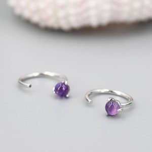 May include: A pair of silver hoop earrings with small purple amethyst gemstones.