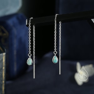 May include: A pair of silver chain earrings with turquoise teardrop-shaped stones hanging from the bottom. The earrings are on a black display stand.