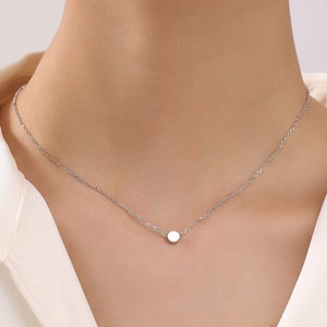Puede incluir: Un delicado collar de cadena de plata con un pequeño colgante redondo.
