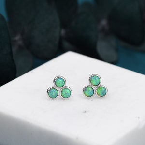 May include: A pair of silver earrings with three green opal stones arranged in a triangular shape.