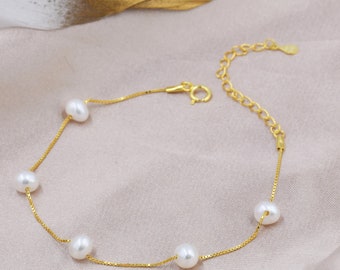 Peut inclure: Un bracelet délicat en chaîne dorée avec cinq perles blanches. Le bracelet est doté d'un fermoir à mousqueton.