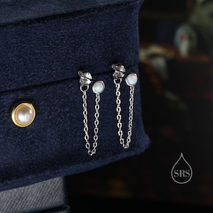 May include: A pair of silver chain earrings with opal stones. The earrings are hanging from a blue velvet box.