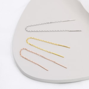 May include: Three pairs of delicate chain earrings in silver, gold, and rose gold. Each pair features a thin chain with a straight bar at the end.