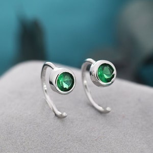May include: A pair of silver hoop earrings with a single green gemstone in each hoop.