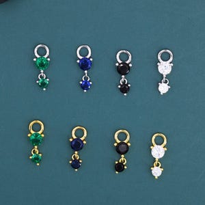 Puede incluir: Una colección de colgantes de piedras preciosas en varios colores, incluyendo verde, azul, negro y blanco. Cada colgante presenta un pequeño lazo en la parte superior y un diseño colgante con múltiples piedras.