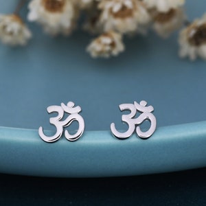 May include: A pair of silver Om symbol stud earrings. The earrings are small and delicate, and they are perfect for everyday wear.
