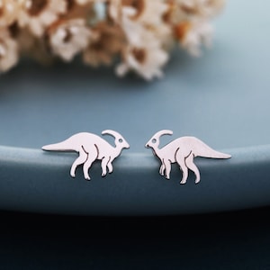 May include: A pair of silver dinosaur earrings. The earrings are shaped like a small dinosaur with a long neck and tail.