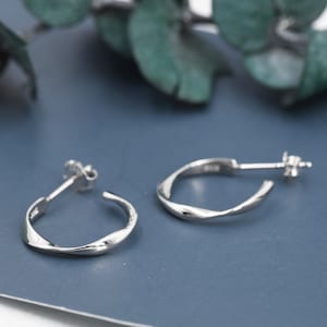 May include: A pair of silver hoop earrings with a twisted design. The earrings are on a blue surface.