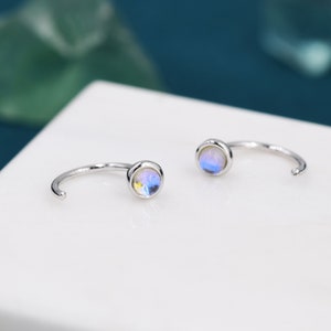 May include: A pair of silver hoop earrings with iridescent blue gemstones. The earrings are simple and elegant, perfect for everyday wear.