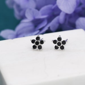 May include: A pair of silver flower stud earrings with black gemstones. Each earring features a five-pointed star shape with six black gemstones.