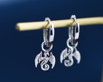 May include: A pair of silver hoop earrings with a dragon charm hanging from each hoop.