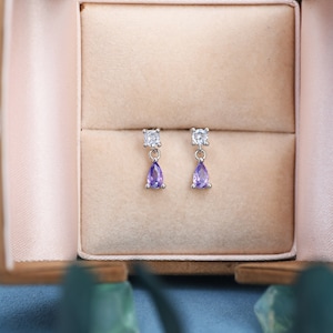 May include: A pair of silver earrings with a small clear gemstone at the top and a larger purple gemstone dangling below.