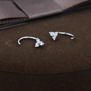 Può includere: Un paio di orecchini a cerchio d'argento con un piccolo gruppo di pietre di zircone cubico trasparenti su ogni cerchio.