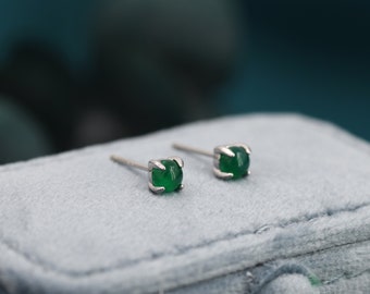 Puede incluir: Un par de pendientes de plata con detalles de piedras preciosas verdes. Los pendientes se muestran sobre una superficie de terciopelo gris.