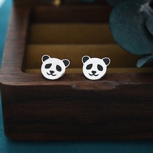 May include: A pair of silver panda bear stud earrings. The earrings are small and round, with a black and white panda bear design.
