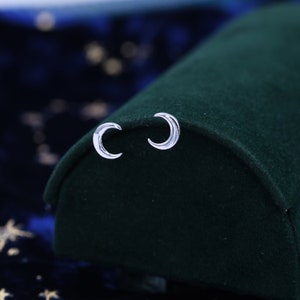 Könnte beinhalten: Ein Paar silberne Halbmond-Ohrringe auf einem grünen Samt-Hintergrund.