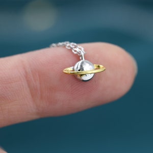 May include: A silver necklace with a gold ring around a silver sphere pendant, resembling a planet with a ring.