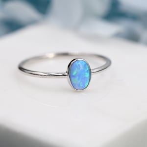 May include: A delicate silver ring featuring a light blue oval opal gemstone.