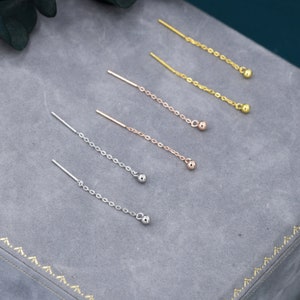 May include: Six pairs of dangle earrings with a small ball at the end of a chain. The earrings are in three different colours: gold, rose gold, and silver.