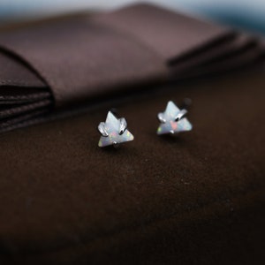 May include: A pair of silver triangle stud earrings with iridescent white opal stones.